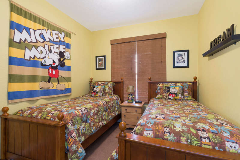 This cheerful themed bedroom  includes these twin beds, a nightstand with lamp, a dresser with 20-inch flat-screen, wall-mounted TV, and closet space and is decorated with Mickey Mouse themed motifs.