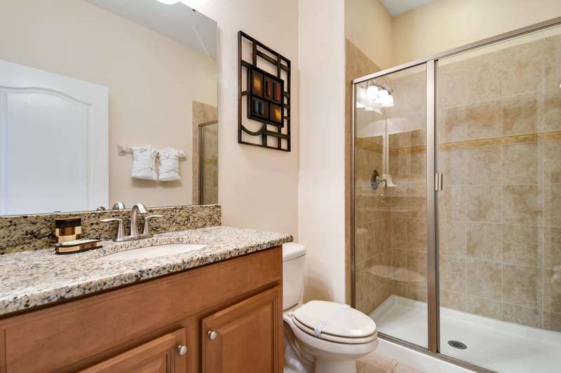 This spacious bathroom is located next to the downstairs bedroom and is also accessible from the hallway as a family bathroom. It has a walk-in shower, a mirrored vanity unit with an under-mounted basin set in a granite worktop and a toilet.